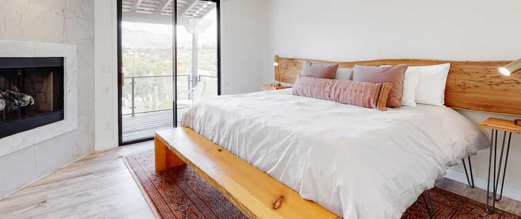 Inside a Tucson, AZ vacation rental bedroom with a white bed, wooden style furniture and fireplace.