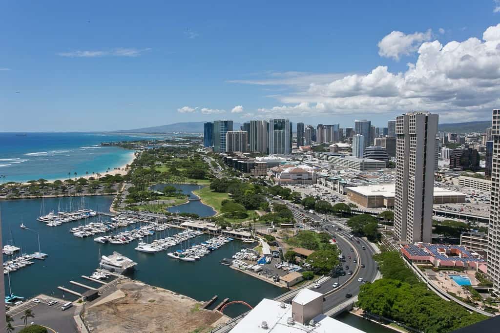 City of Honolulu, HI with sky scrapers, busy roads, a beach shoreline, and a marina with rows of boats.