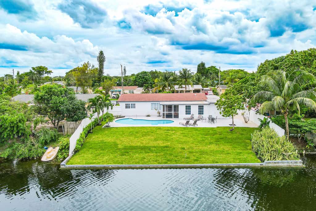 A drone shot of the back yard of a vacation rental with a pool and large deck near the water in Deerfield Beach, FL.