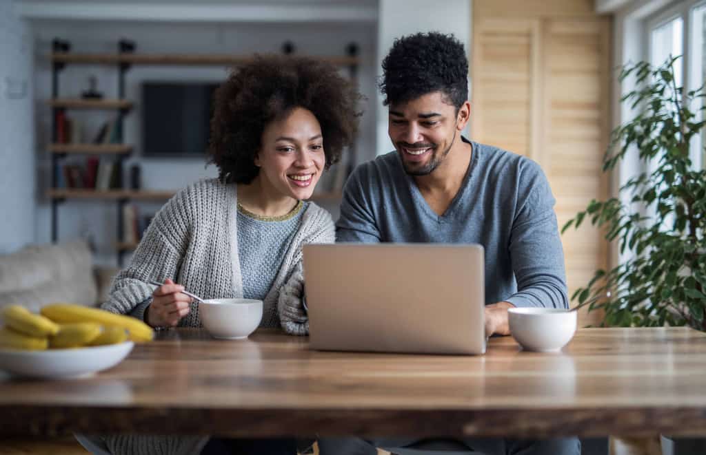 a couple drinking coffee looking at their laptop