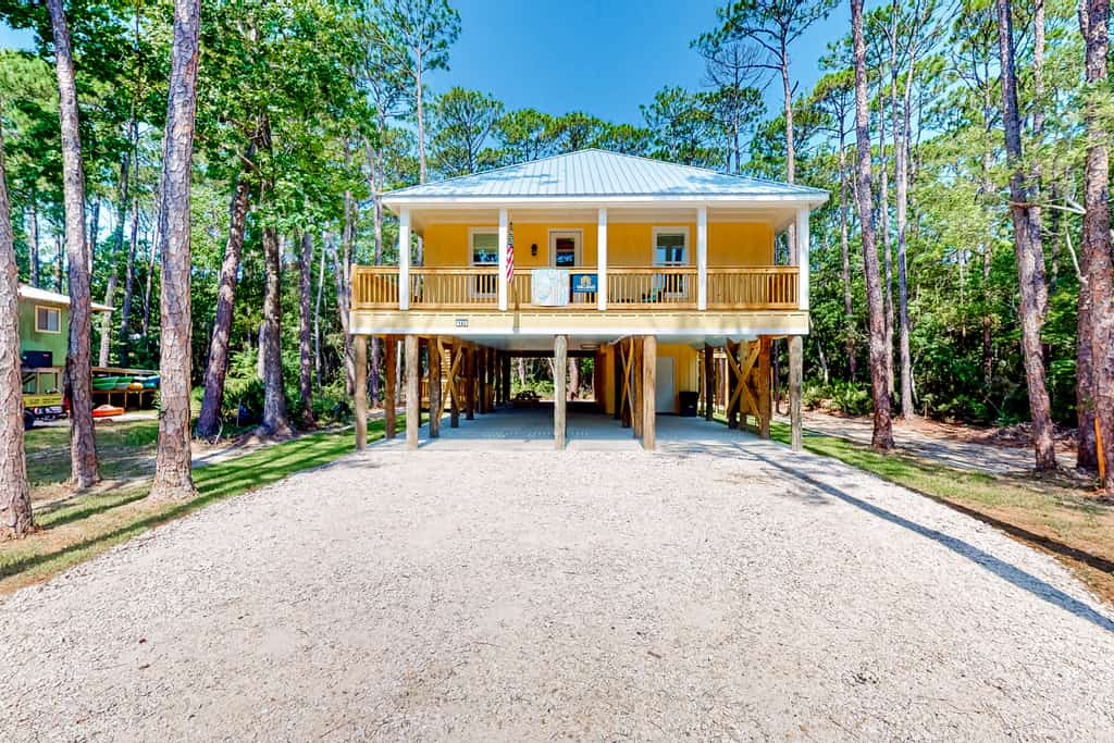 The front of a vacation rental in Dauphin Island, AL surrounded by trees and near the beach.
