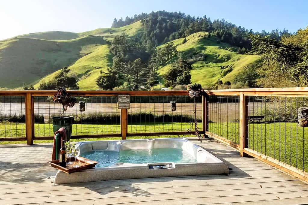 private outdoor hot tub at a vacation home in russian river with a wine bottle and two wine glasses on a tray nearby