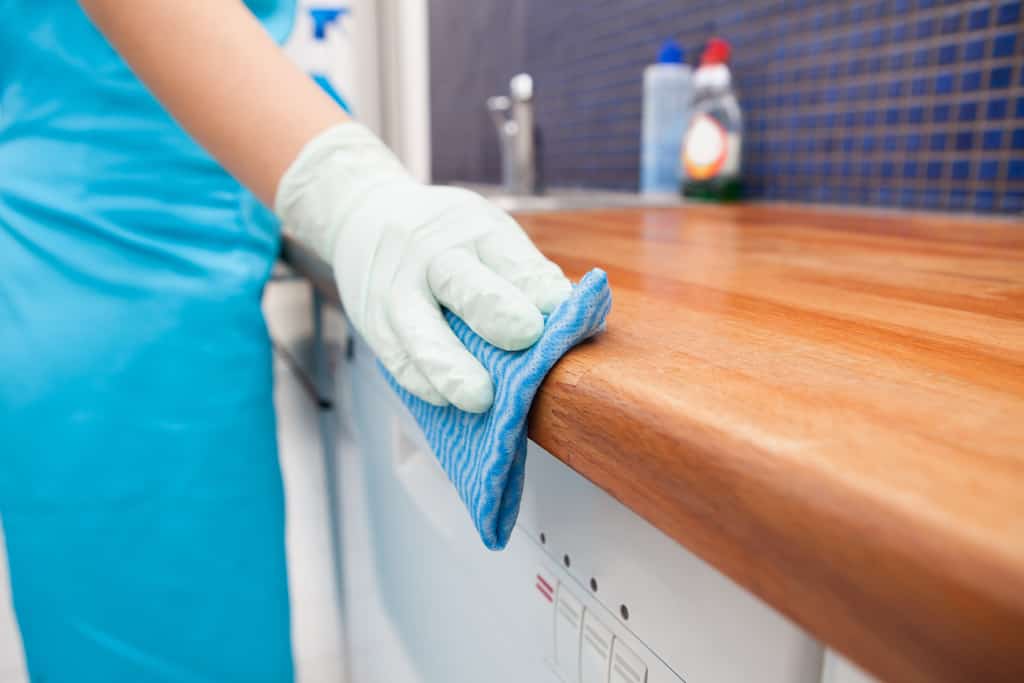 A cleaner wiping down a wooden countertop.