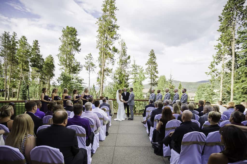 Bride and groom standing at the alter and performing wedding ceremony in front of family and friends at a terrace in BlueSky Breckenridge, CO.