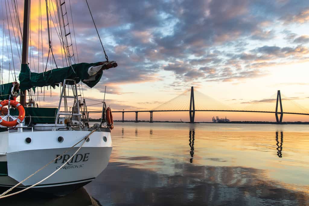 Sailboat moored to a dock on calm water and a bridge in the distance at Charleston Harbor
