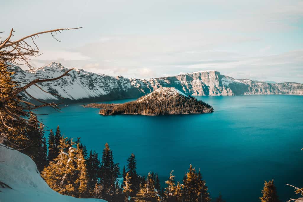 Crater lake during the winter with snow covering the outer rim and Wizard Island with a snowy peak