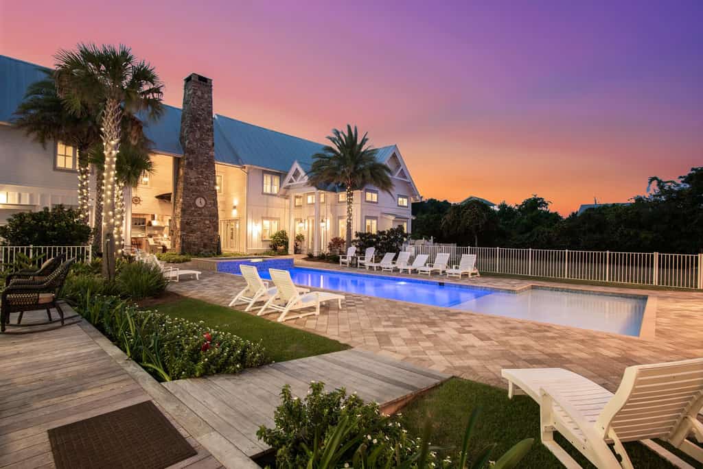 Backyard of a vacation rental with a pool, deck chairs, and a gorgeous house.