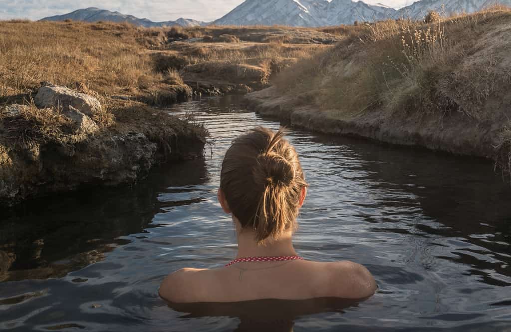 A woman in a narrow river stream facing mountains in McCall, ID.