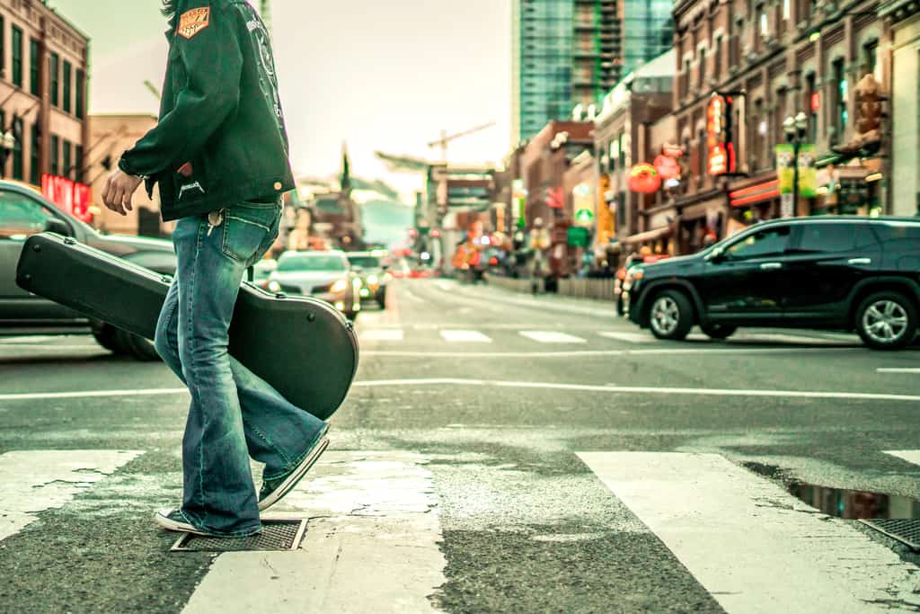man with guitar crossing the street