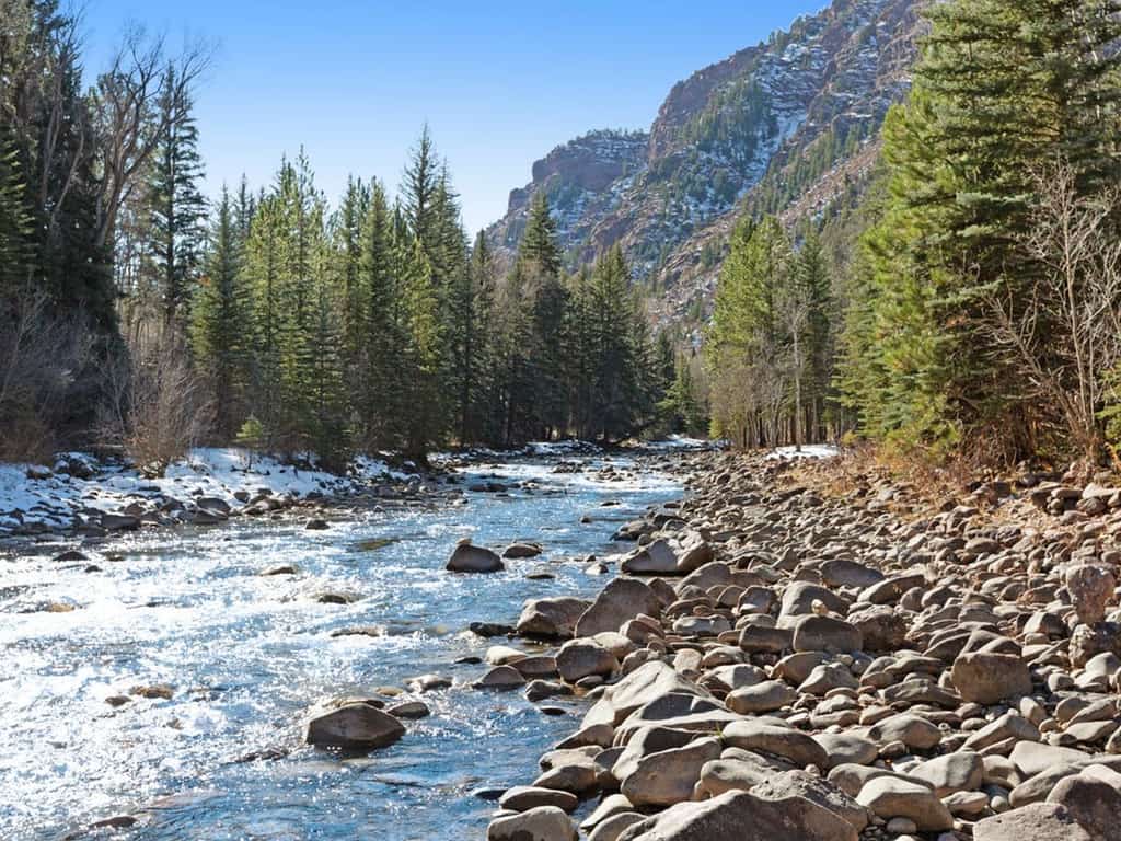 Rushing river in Colorado surrounded by trees and mountains.