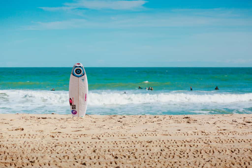 a single surfboard sticks out of the sand in front of the ocean on a beautiful sunny day