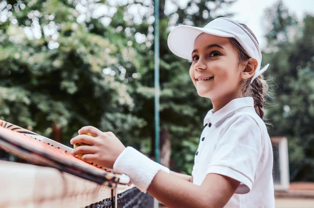 young girl dressed for a game of tennis holds tennis racket and ball