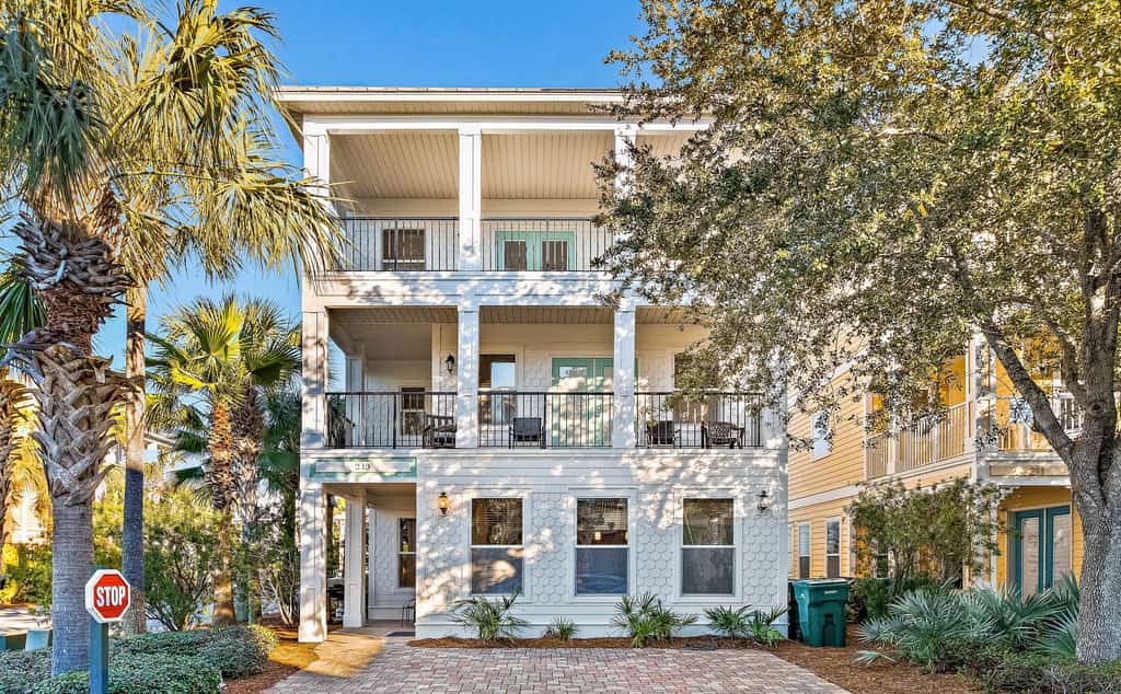 Three story vacation rental with a brick driveway during the day.