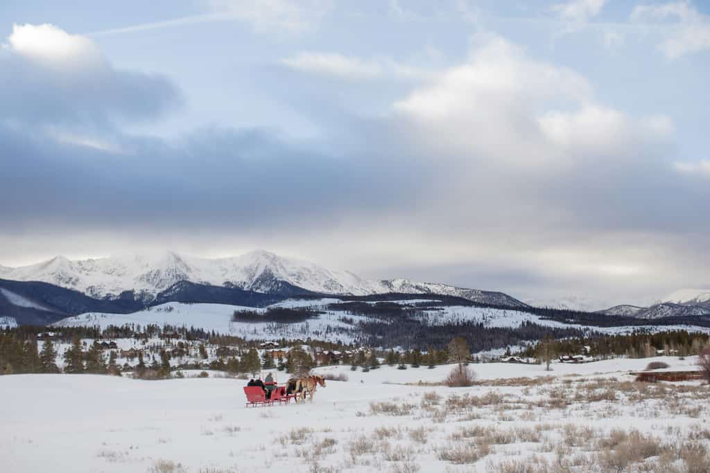 red horse-drawn carriage ride in breckenridge in winter surrounded by snow covered mountains