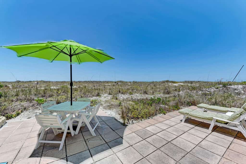 a patio with a table and beach chairs overlooking the sand dunes