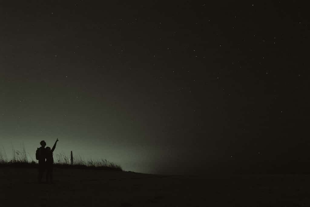 Two kids pointing at the stars in the dark.