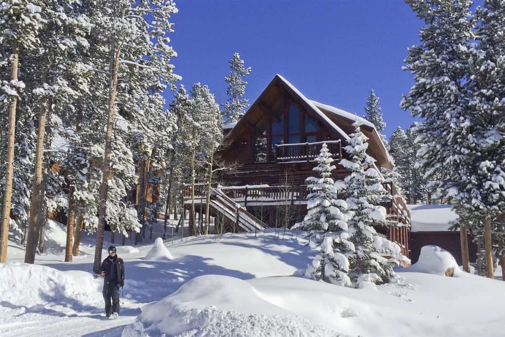 man poses in the snow in front of his breckenridge, co cabin rental