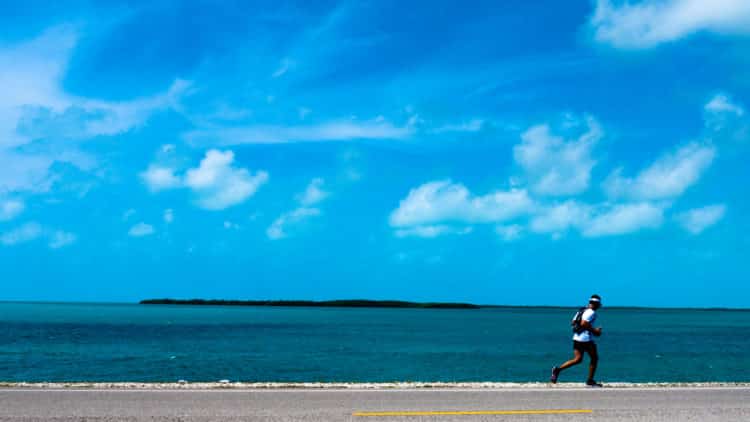 Person jogging alongside a road by the ocean on a sunny day in Florida Keys.