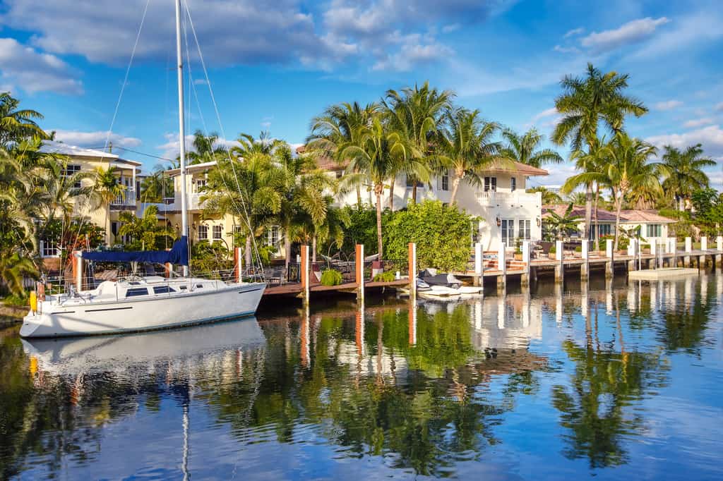 A view of the bay in Fort Lauderdale FL with palm trees, vacation home rentals and a sail boat.