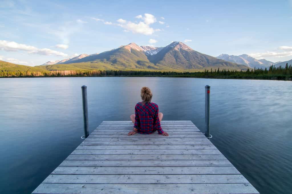 woman sitting at the end of a dock overlooking a lake and mountains