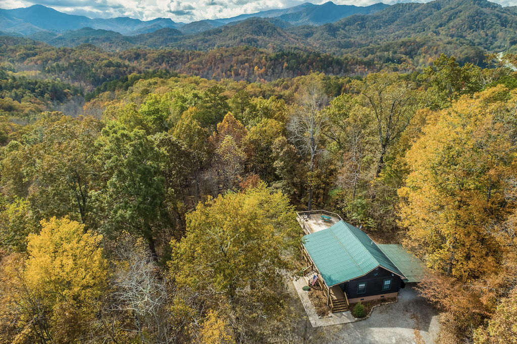 cabin with green roof surrounded by fall trees with mountains in the background in nantahala national forest