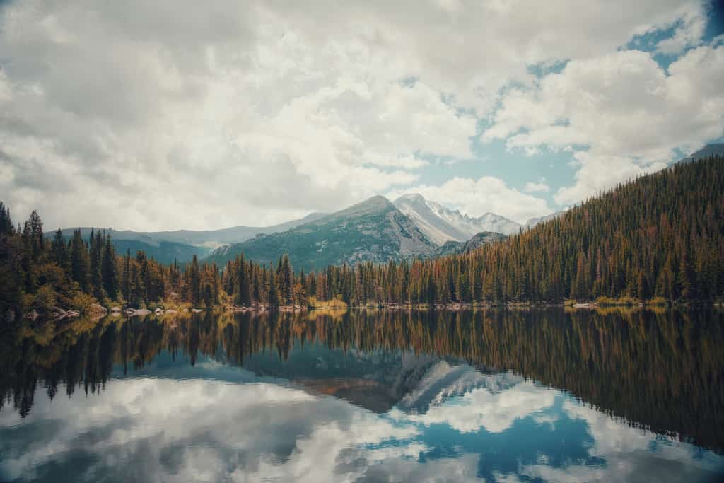pine trees surround lake on a cloudy day with mountain looming in background