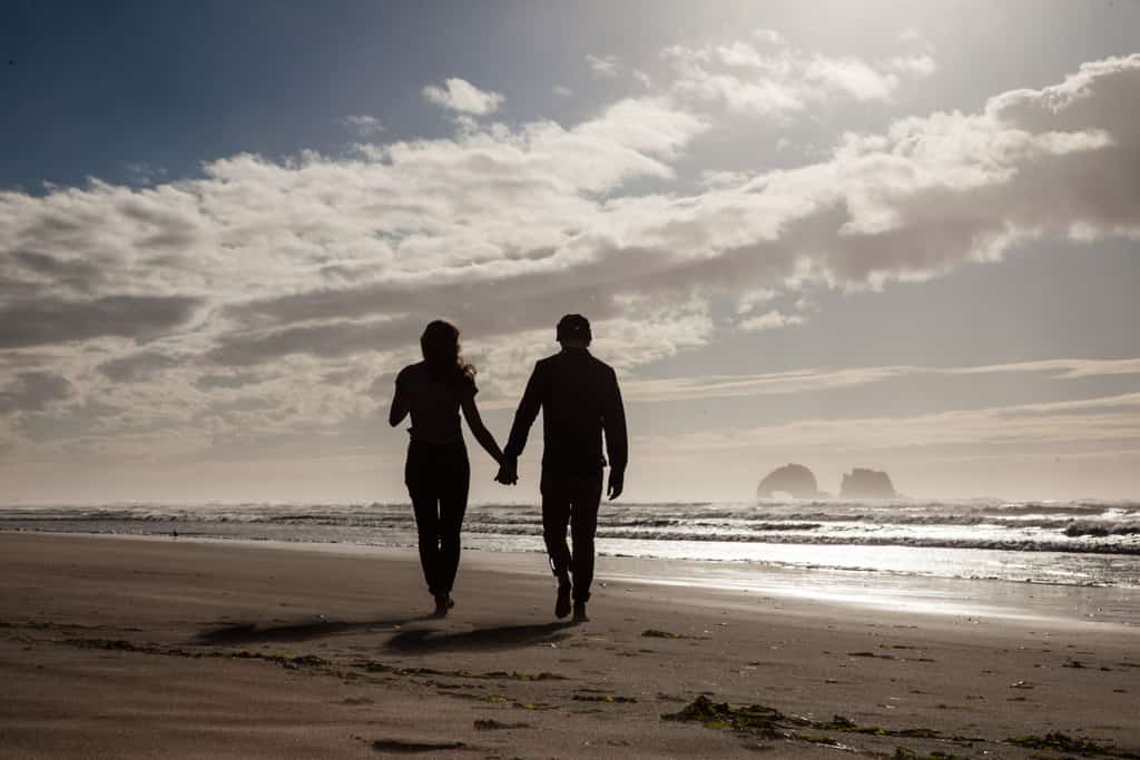 a couple holding hands walking along an oregon beach