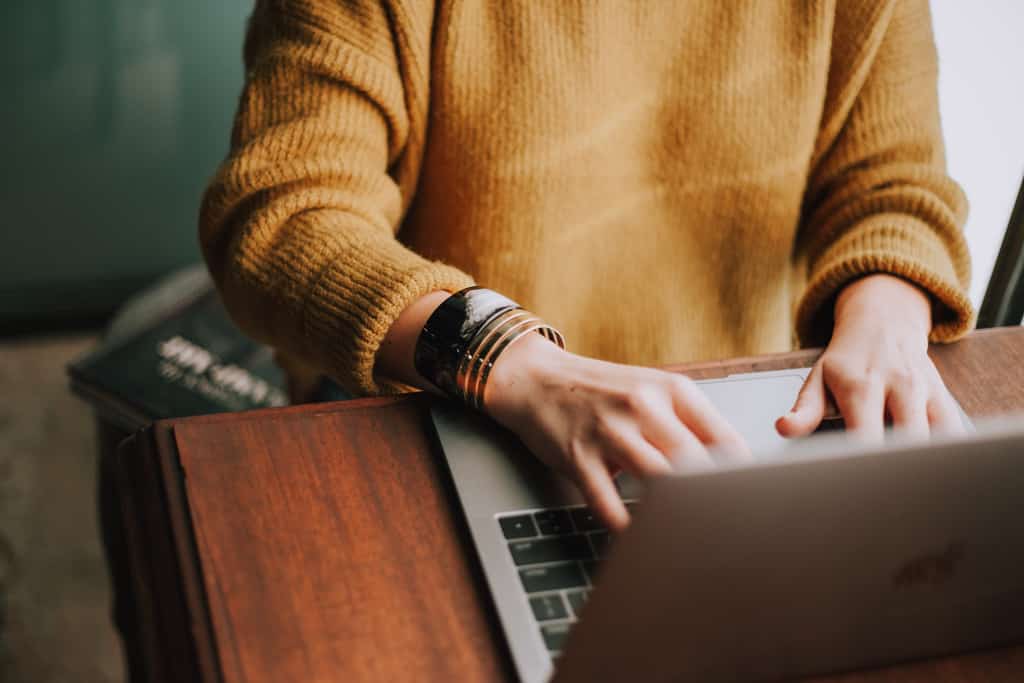 person in yellow sweater and bracelets typing on laptop