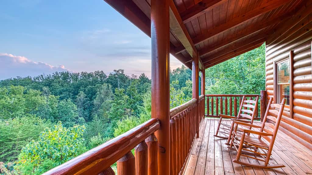 Two wooden rocking chairs on a deck at a cabin overlooking a mountain full of green trees in Tennessee